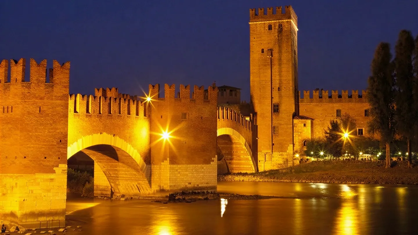 Castelvecchio e il Ponte Scaligero illuminati di notte, con le luci dorate riflesse nell'Adige